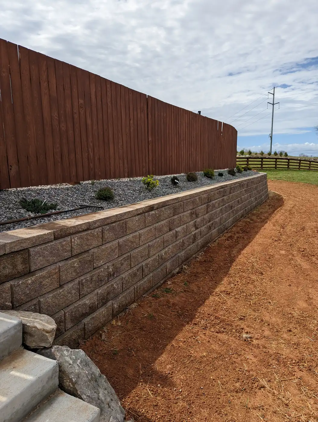 Block retaining wall with a planting bed along a wood fence in Nashville, TN