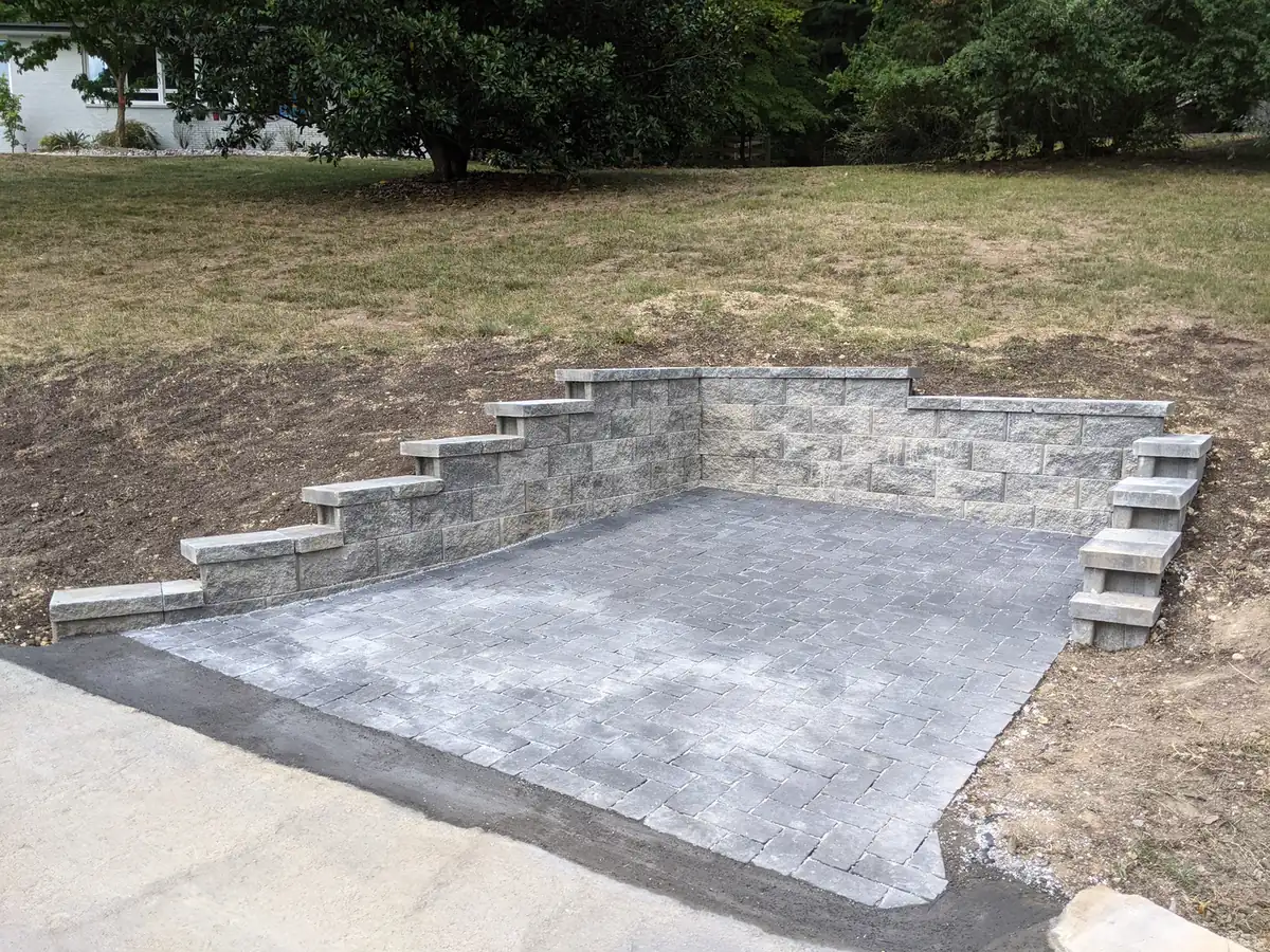 Block retaining wall with steps around a concrete pad on a sloped lot in Nashville, TN