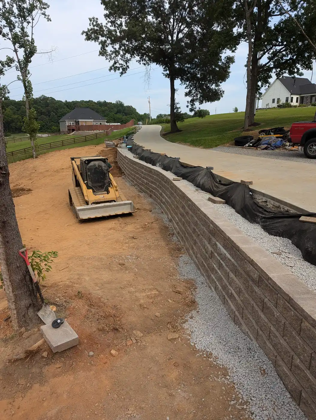 Block retaining wall along a driveway with skid steer and drainage fabric in Nashville, TN