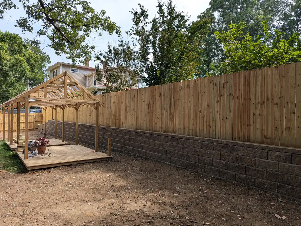 Block retaining wall topped with a wood fence beside a timber pavilion under construction in Nashville, TN