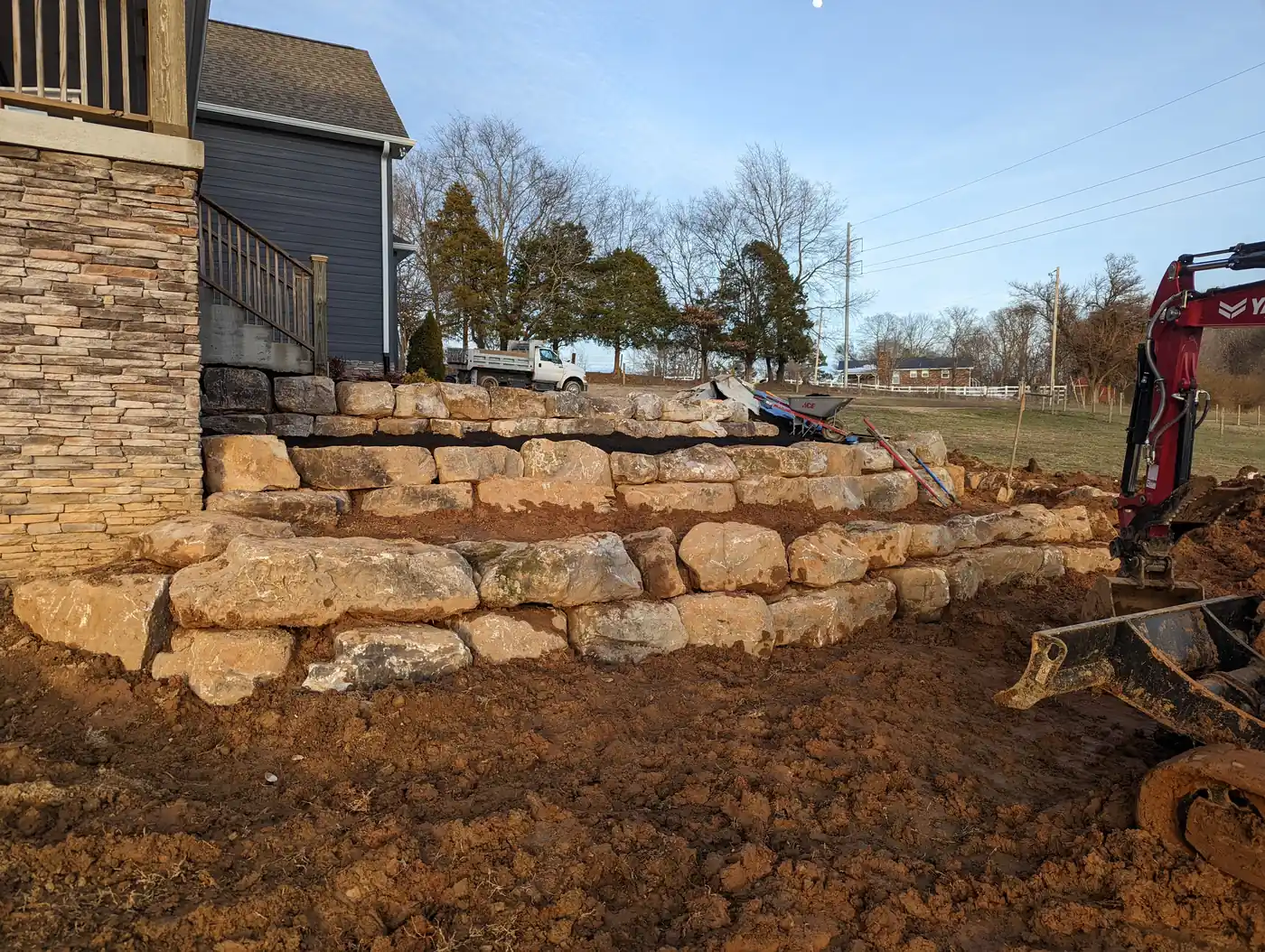 Boulder retaining wall being set with an excavator beside a stone home in Nashville, TN