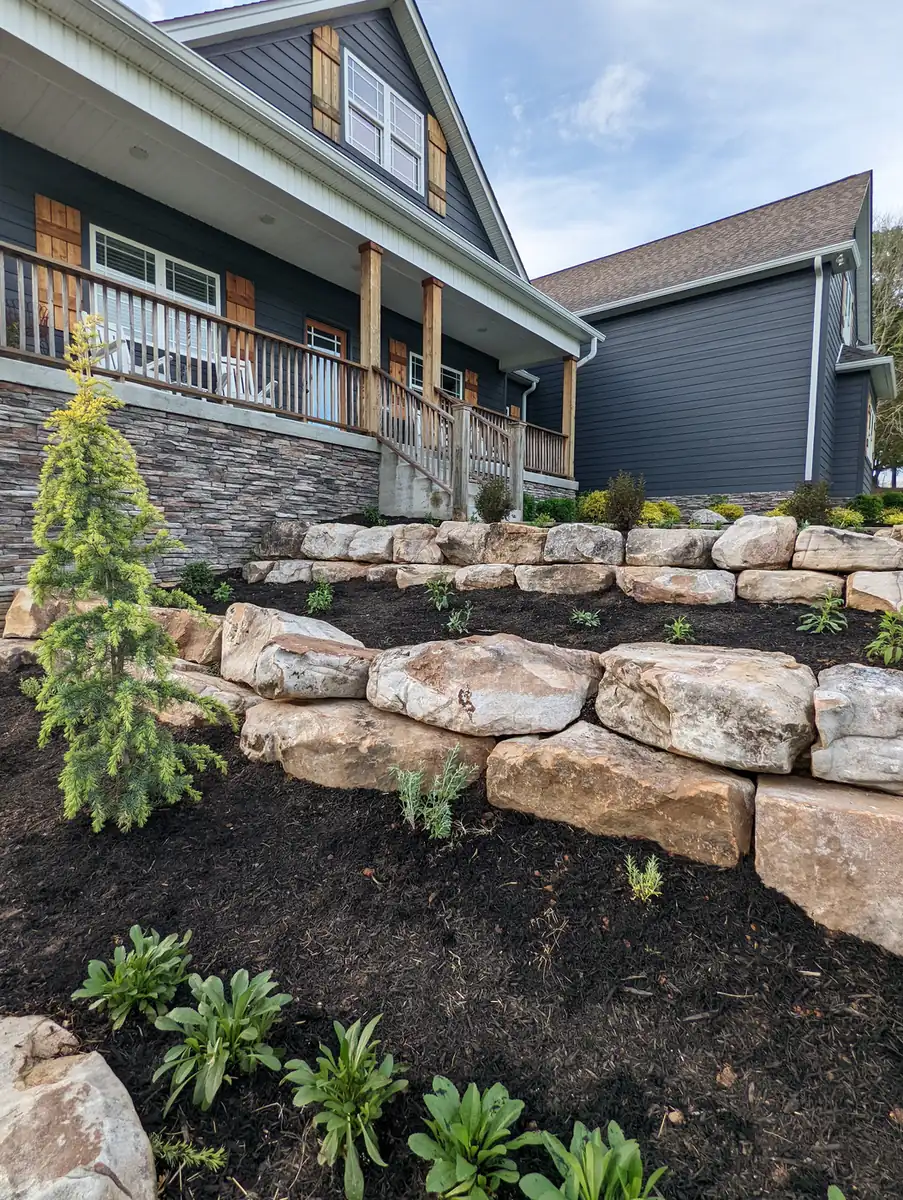 Boulder wall terraces planted with evergreens and perennials at a stone and blue home in Nashville, TN