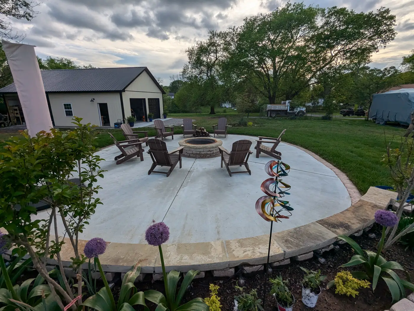 Circular concrete patio with fire pit and Adirondack chairs framed by flower beds in Nashville, TN