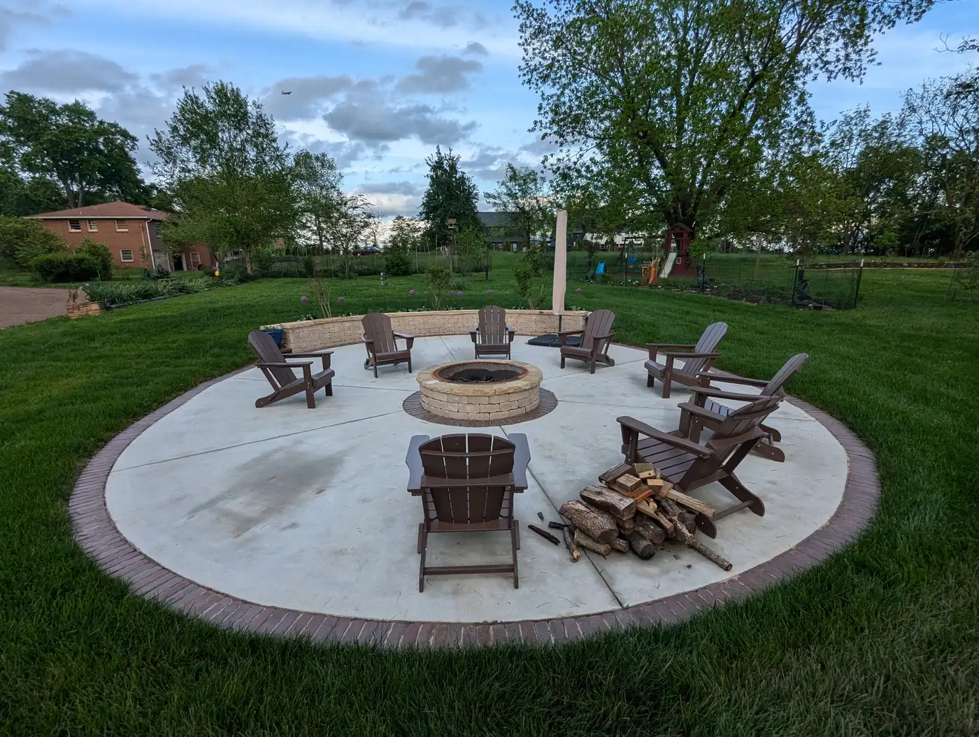 Circular fire pit patio with dark Adirondack chairs and stacked firewood in Nashville, TN
