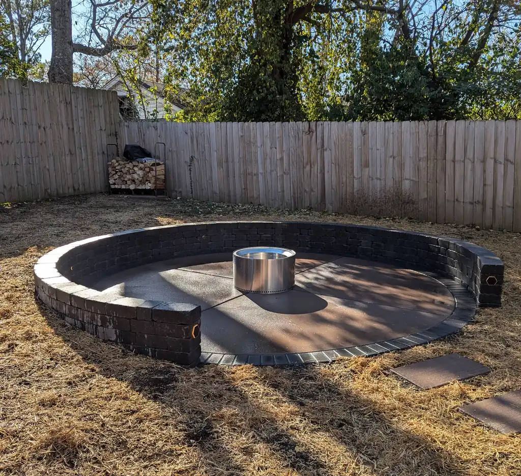 Round concrete fire pit patio wrapped by a dark block seating wall in a fenced Nashville, TN yard