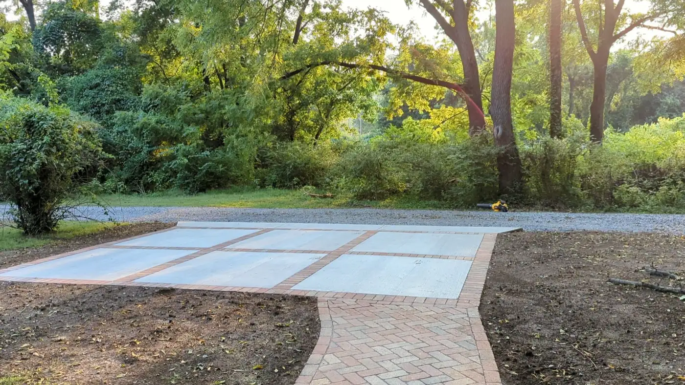 Poured concrete patio with scored panels and a brick paver border in a wooded Nashville, TN backyard
