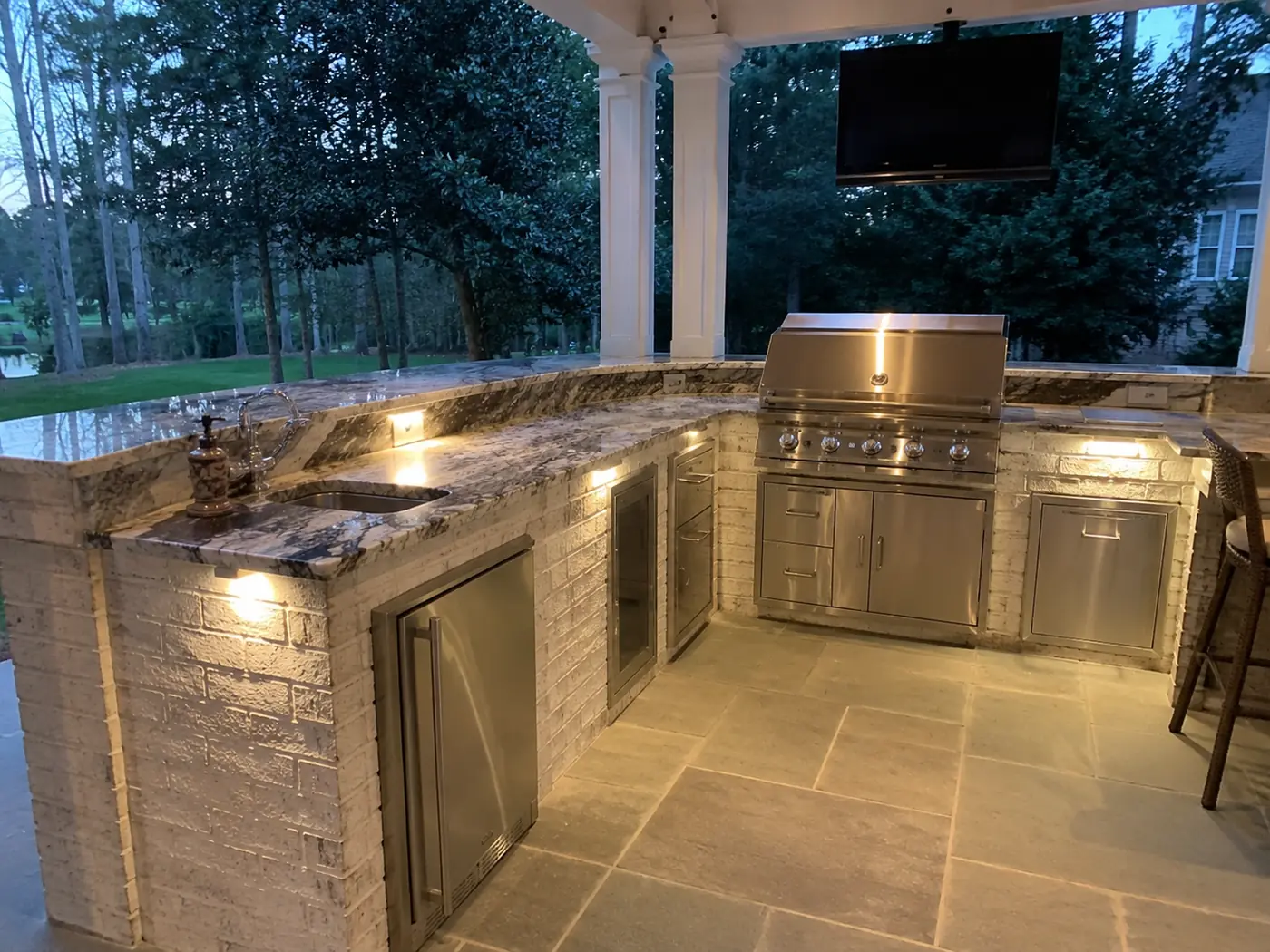 Covered outdoor kitchen with granite counters, grill and TV at twilight in Nashville, TN