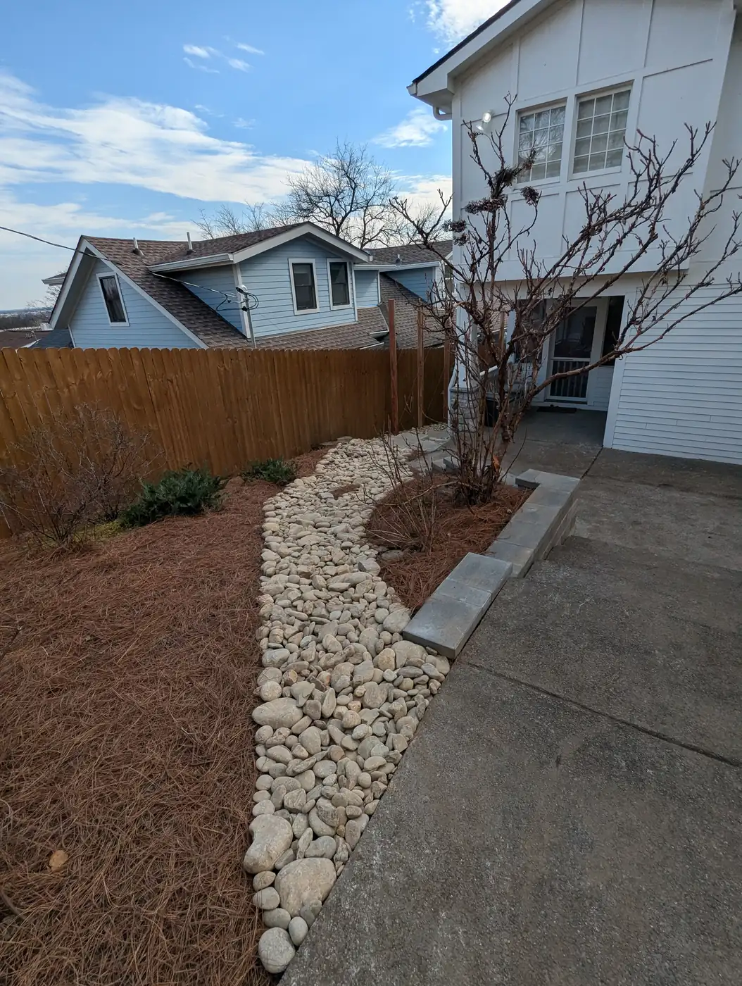 River rock dry creek bed channeling runoff beside a concrete walkway at a white home in Nashville, TN