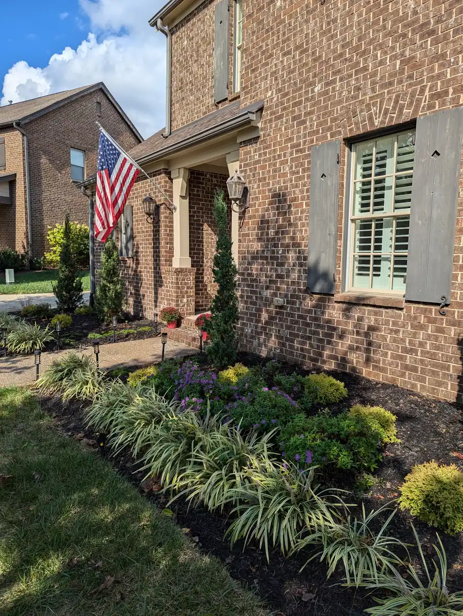 Foundation planting beds with fresh mulch at a brick home with an American flag in Nashville, TN