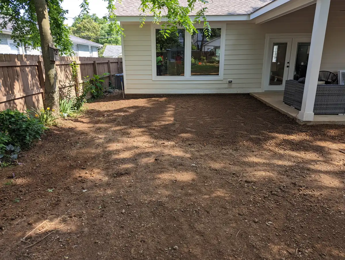 Backyard regraded to bare soil for drainage correction behind a white home in Nashville, TN