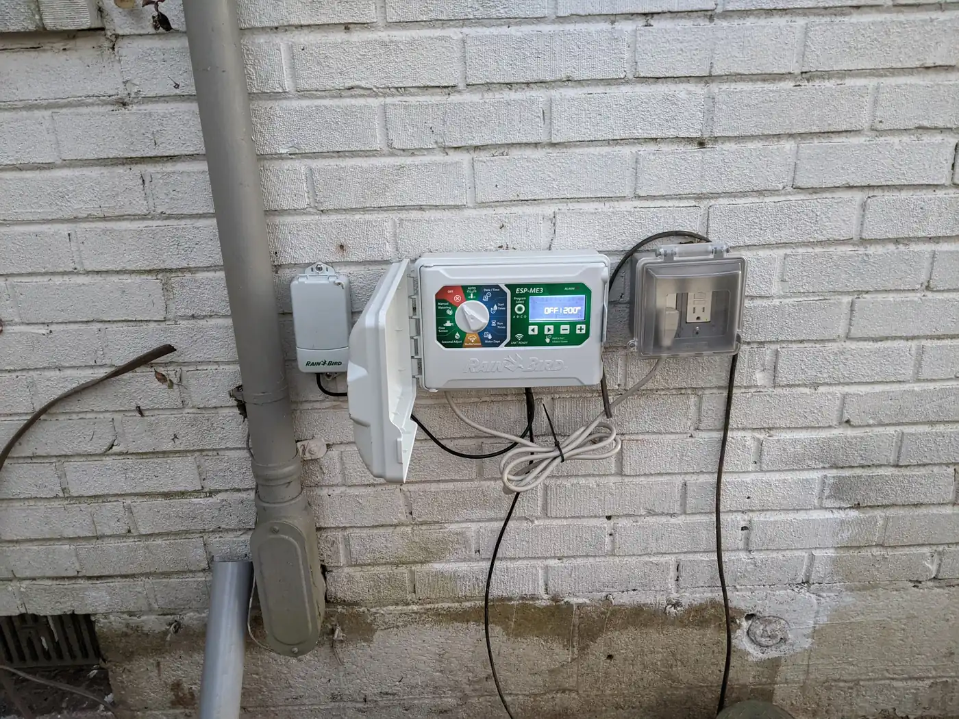 Irrigation controller and rain sensor mounted on a white brick wall in Nashville, TN