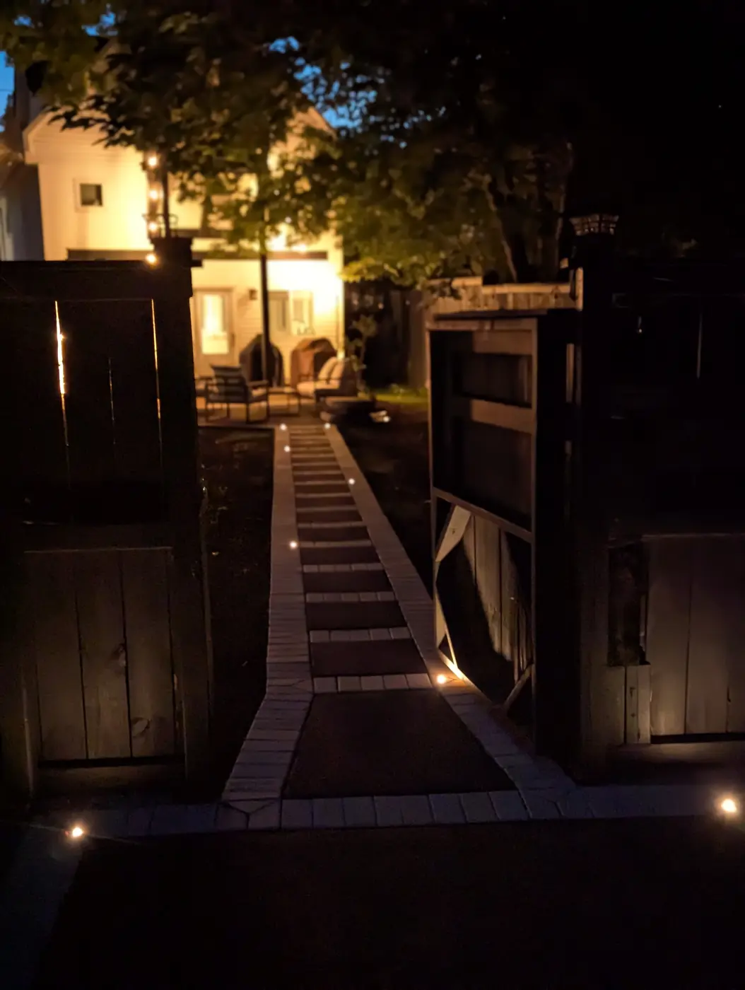 Lit paver walkway between wood fences leading to a home at night in Nashville, TN