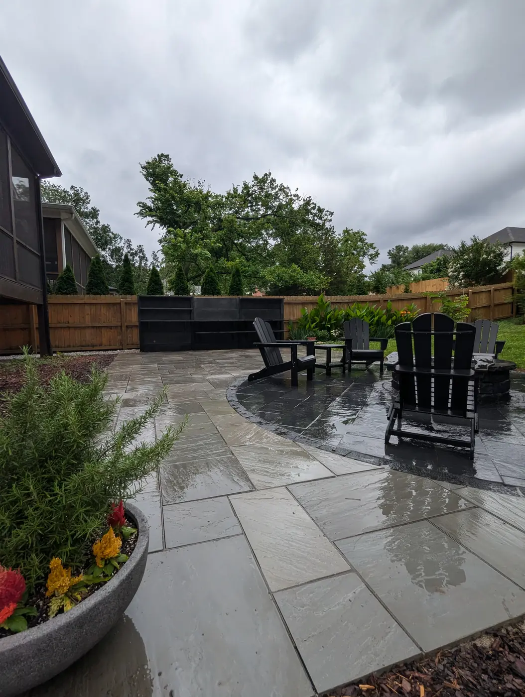 Paver patio with black Adirondack chairs and planter behind a dark modern home in Nashville, TN