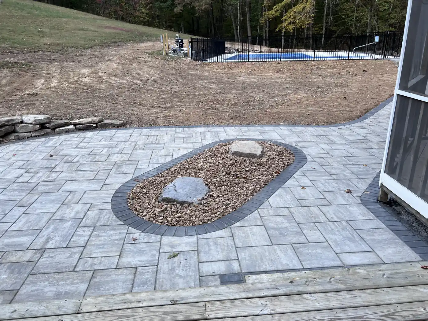 Paver patio with a boulder planter inset and dark border beside a pool in Nashville, TN