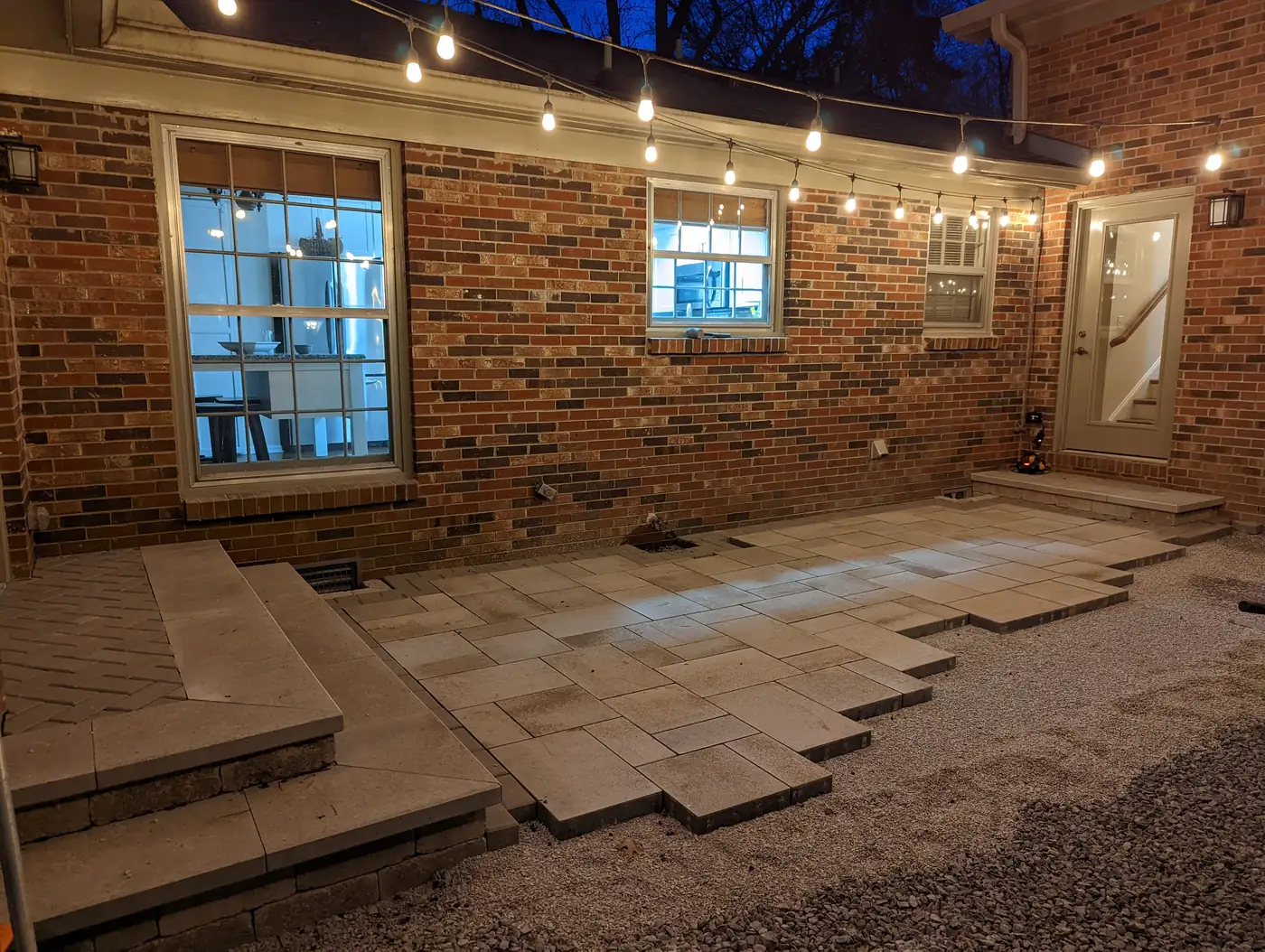 Paver patio being laid beside a brick home with steps and string lights at night in Nashville, TN