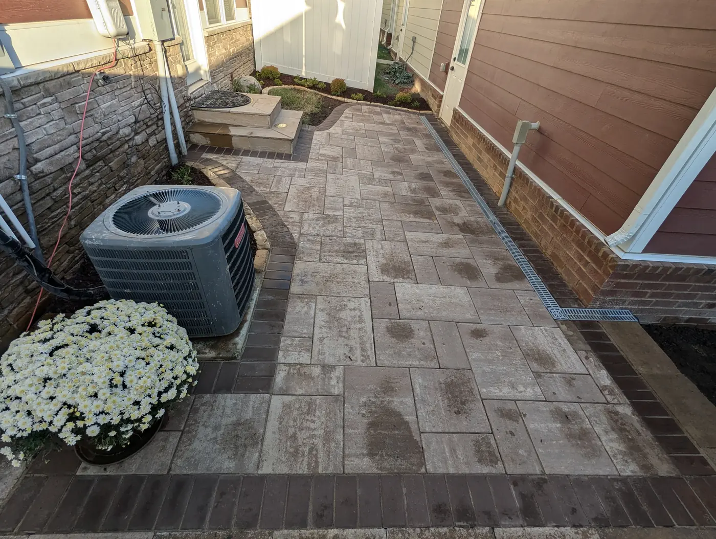Mixed-size paver patio beside the AC unit of a red home with fall mums in Nashville, TN
