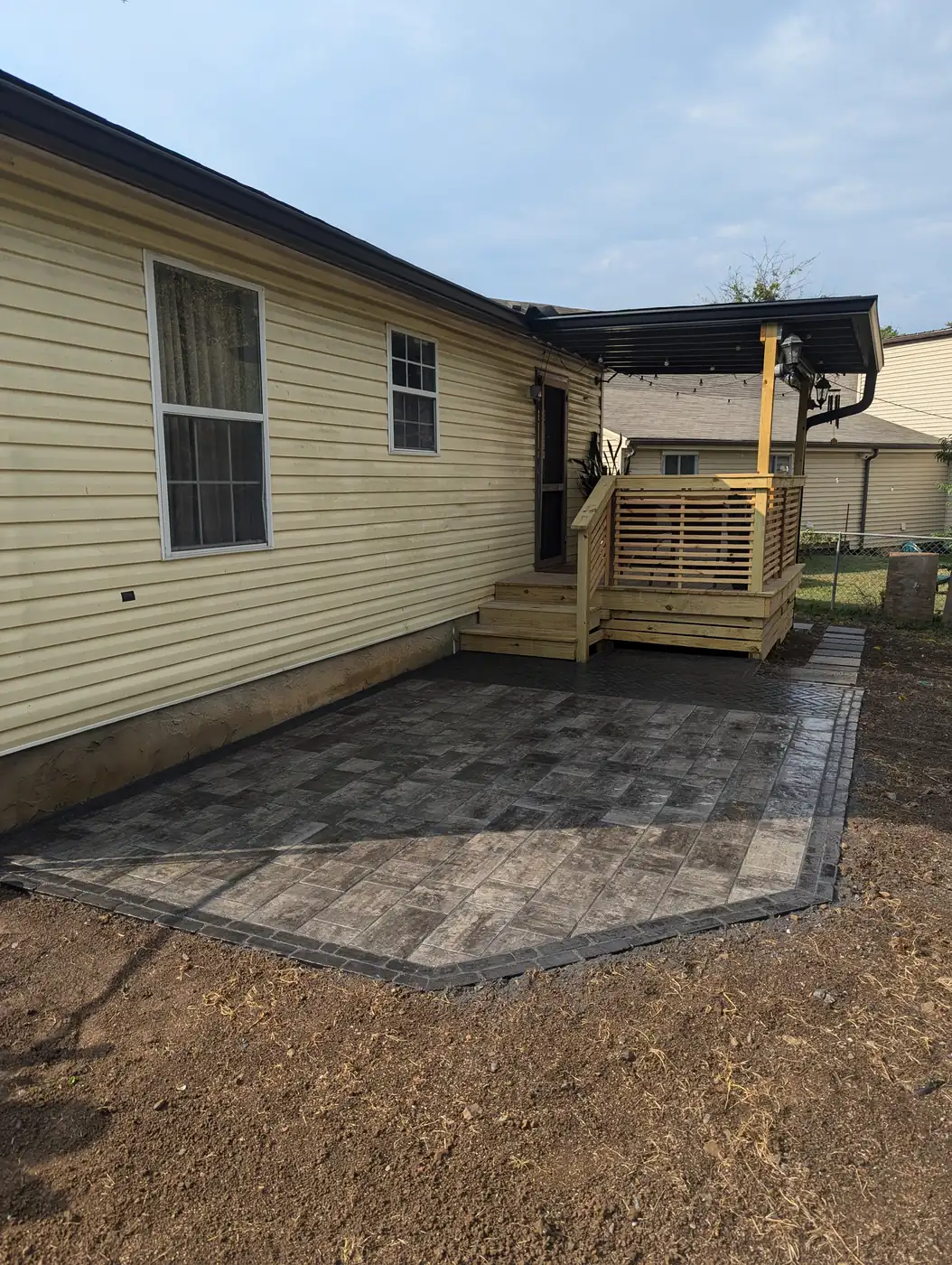 Paver patio at the back of a yellow home beside a wood deck in Nashville, TN