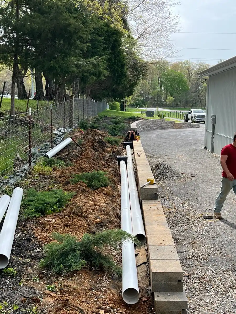 PVC drain pipe staged along a gravel driveway and wall trench for a drainage install in Nashville, TN