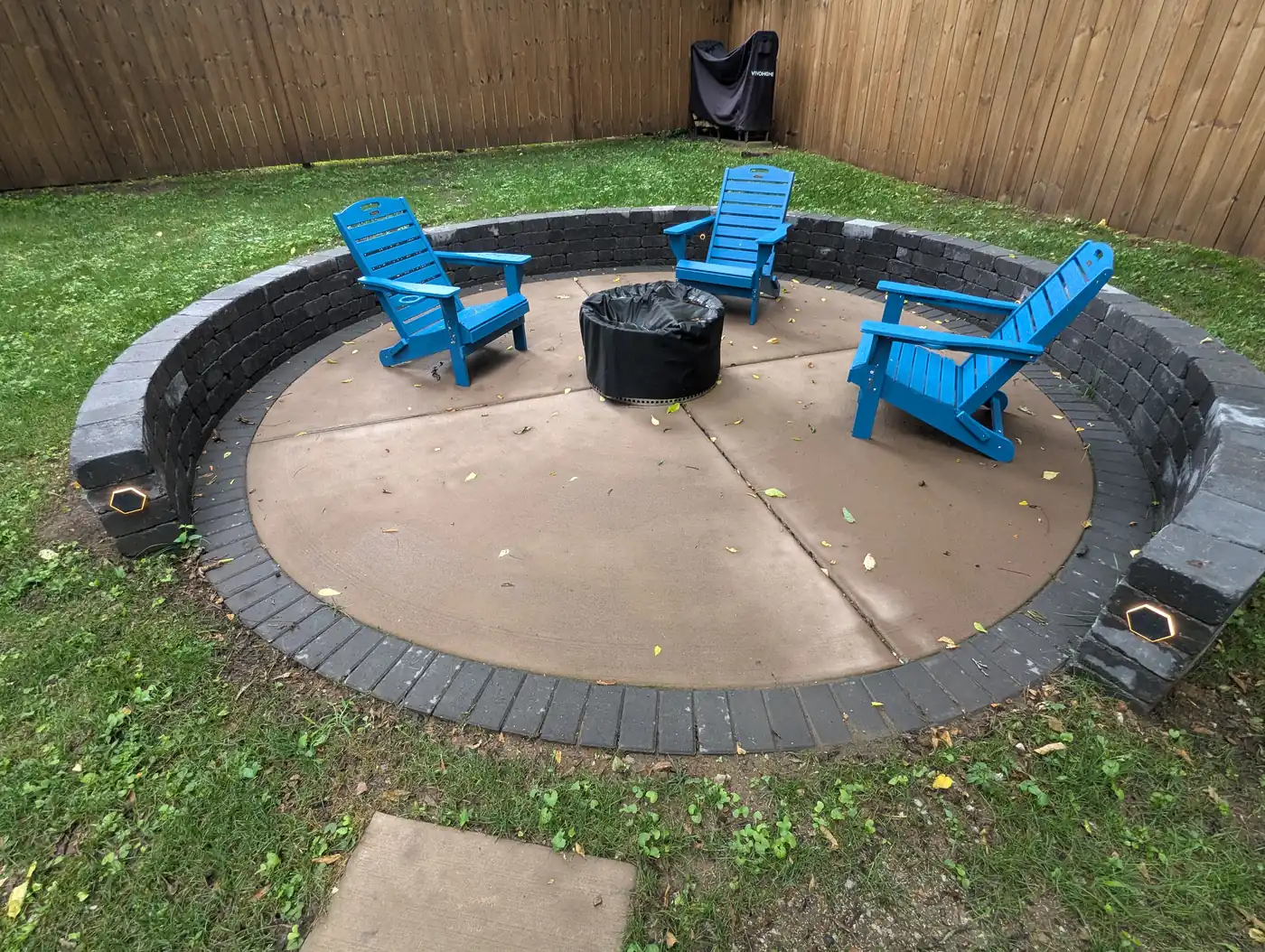 Round concrete patio with a dark paver ring, fire pit and blue Adirondack chairs in Nashville, TN