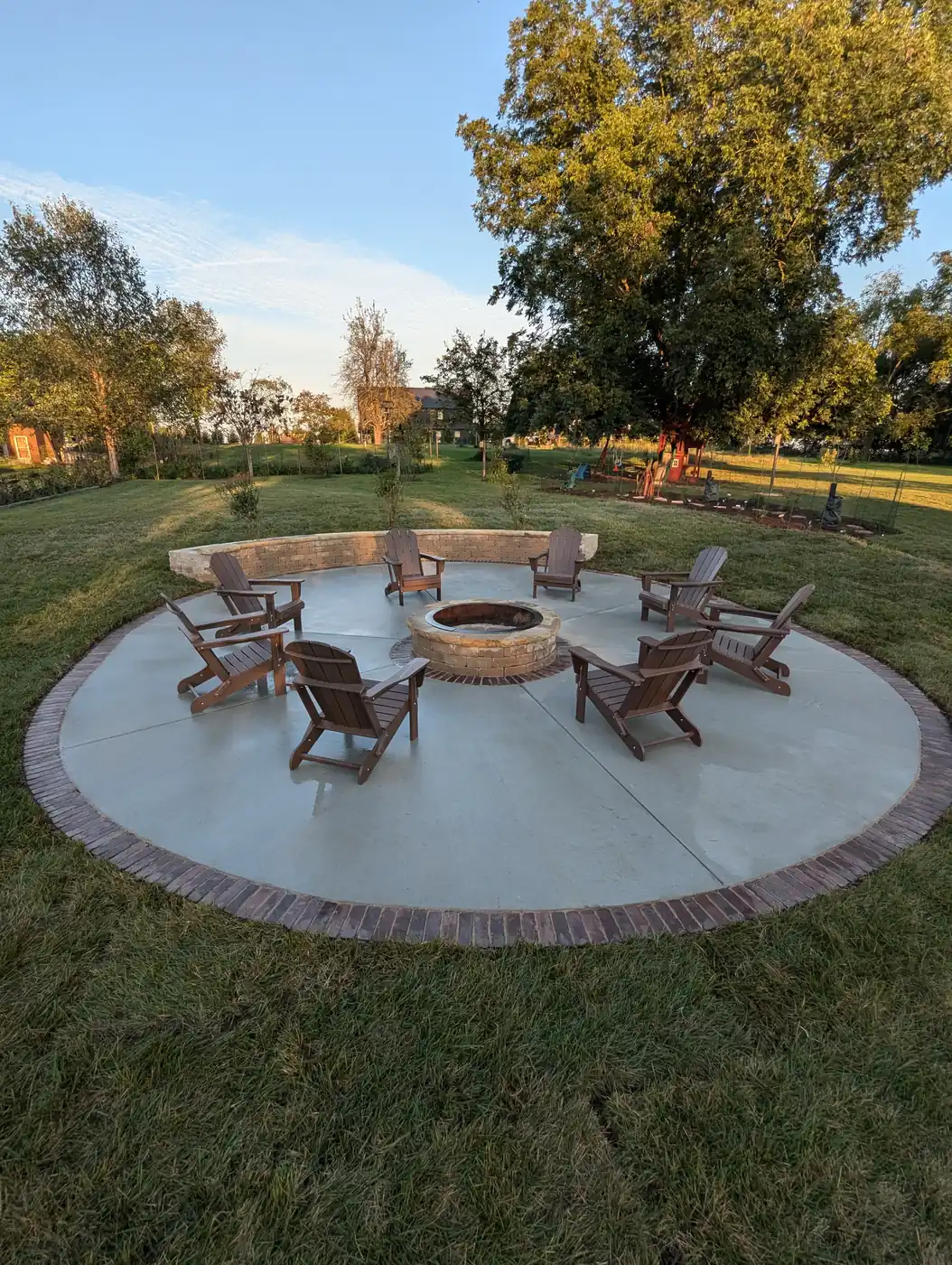 Circular concrete patio with a stone fire pit and brick paver border under a large tree in Nashville, TN