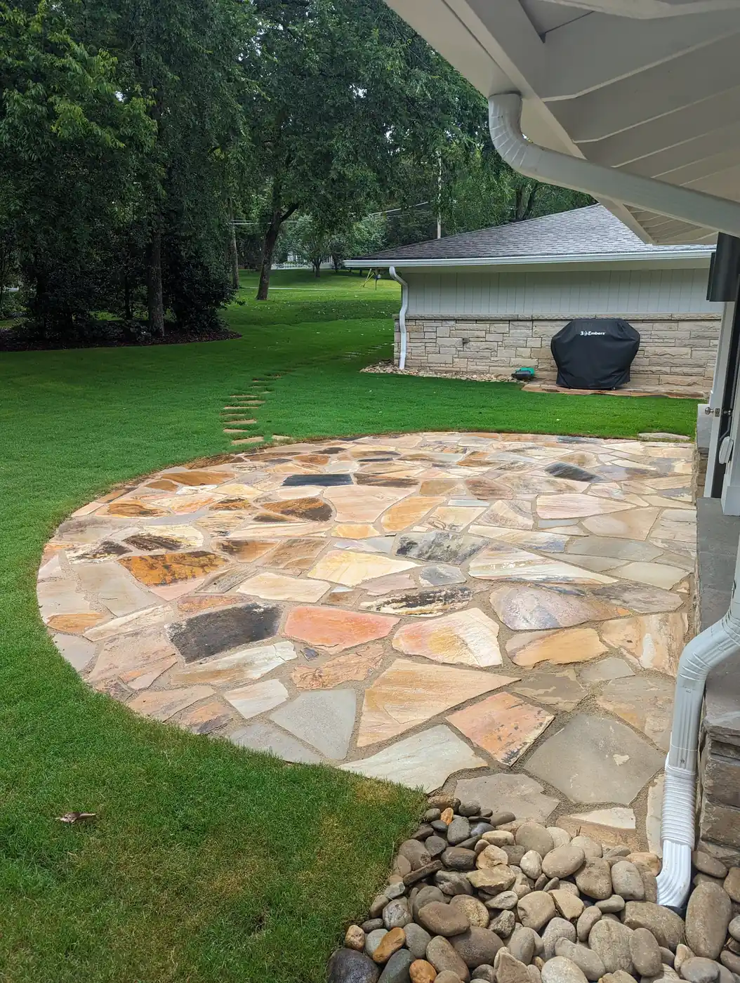 Round flagstone patio with a river rock edge on the lawn of a stone home in Nashville, TN