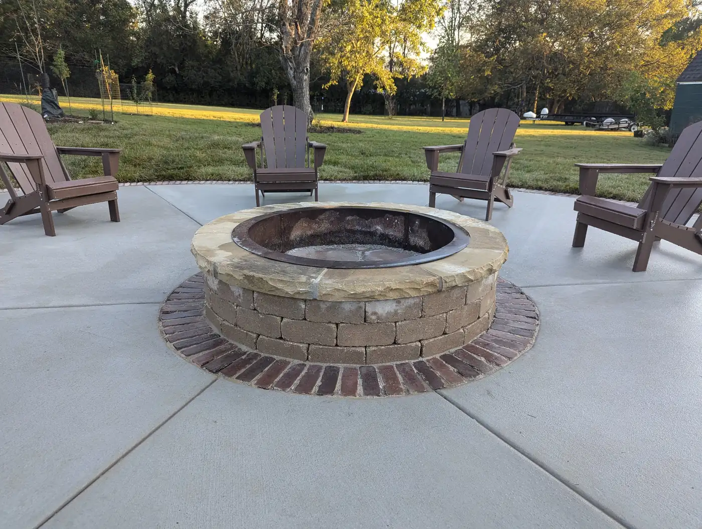 Round stone fire pit on a concrete patio with brown Adirondack chairs in Nashville, TN