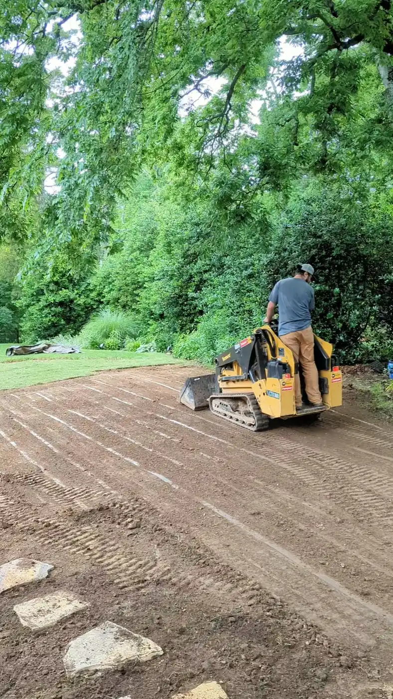 Skid steer regrading a shaded backyard to fix drainage in Nashville, TN