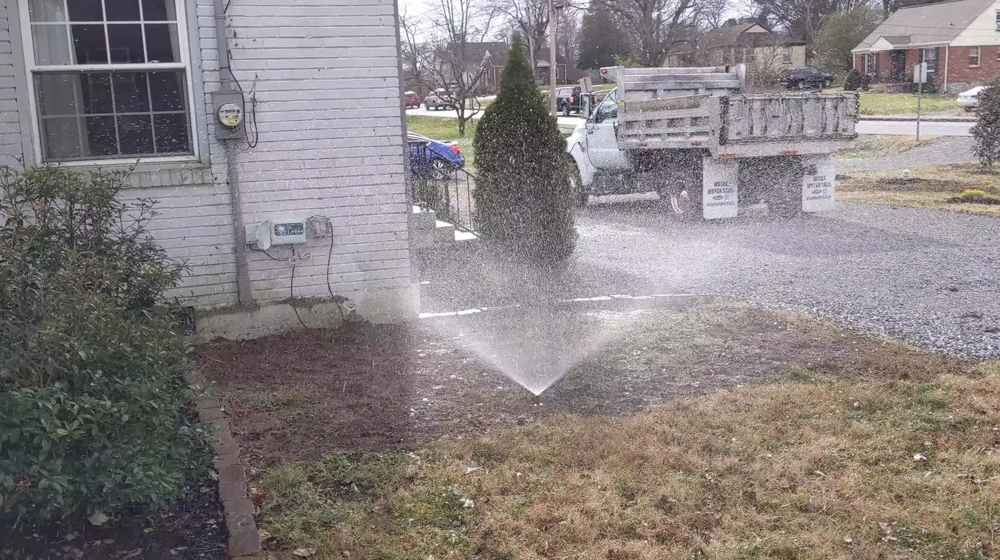 Sprinkler system running on a front lawn beside a white brick home in Nashville, TN