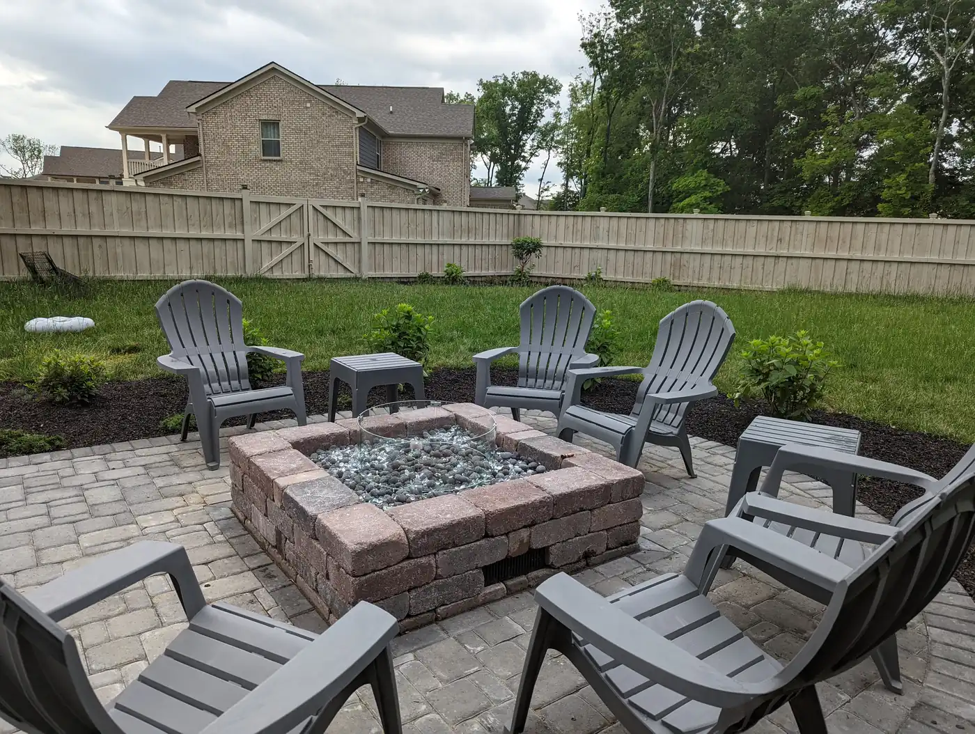 Square paver fire pit with gray Adirondack chairs in a fenced Nashville, TN backyard
