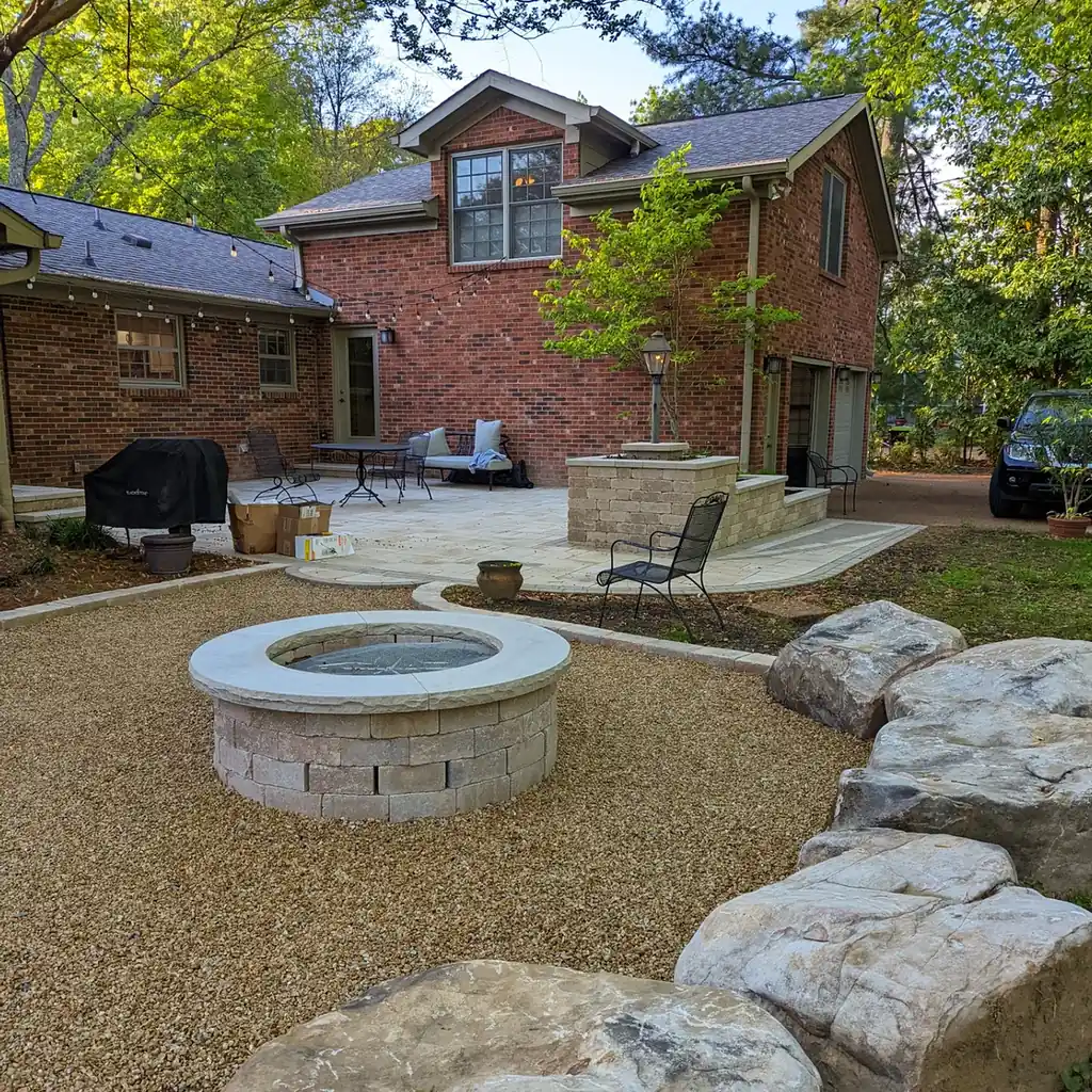 Round stone fire pit on a pea gravel patio with boulders behind a brick home in Nashville, TN