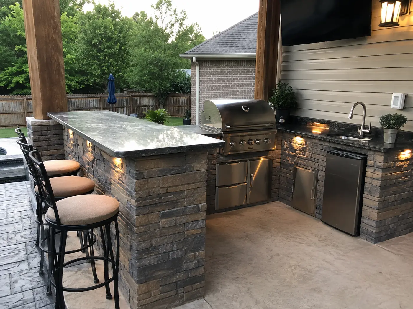 Stone outdoor kitchen bar with grill, fridge and bar stools under a pergola in Nashville, TN