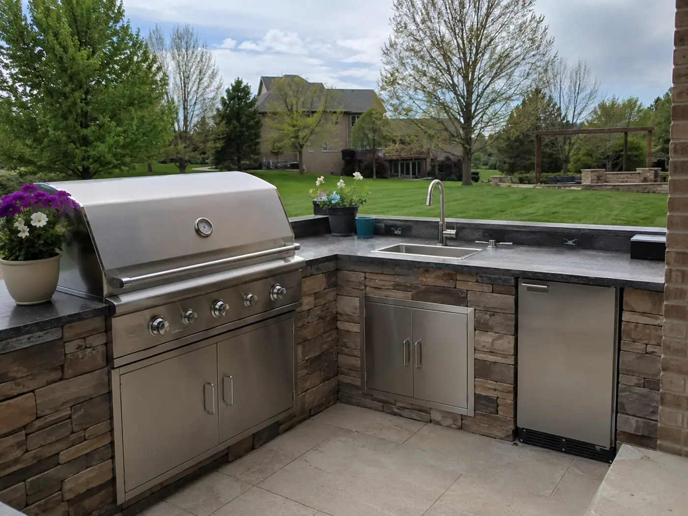 Stone outdoor kitchen with stainless grill and sink overlooking a lawn in Nashville, TN