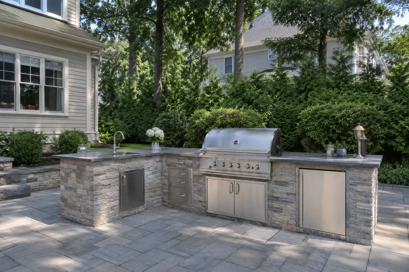 Stone patio outdoor kitchen with a grill island beside a large home in Nashville, TN